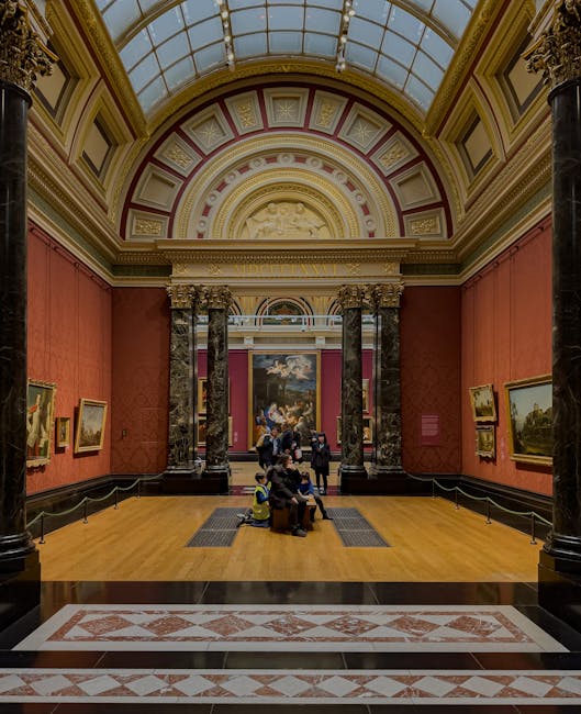 Interior view of a historic art gallery at Tate Britain, featuring a high glass-domed ceiling with intricate molding and decorative details. The walls are covered in textured, reddish-orange wallpaper